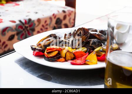 Assiette en céramique blanche avec de délicieuses moules naturelles fraîchement cuites, sauce et légumes biologiques grillés sur fond clair. natur sain Banque D'Images