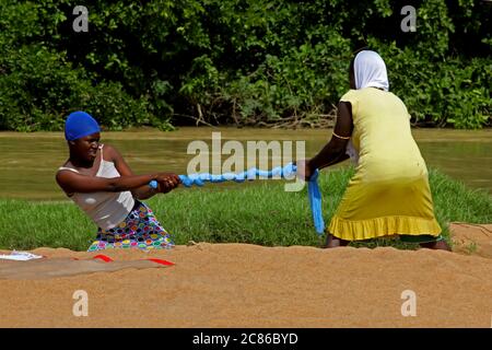 Se faire l'empaque au Ghana. Deux femmes ont essorés un tissu qui vient d'être lavé sur une rive de la rivière. Banque D'Images