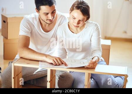 Jeune couple installant des meubles dans une nouvelle maison avec instruction Banque D'Images