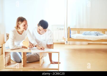 Le couple lit les instructions pour l'assemblage de meubles dans une nouvelle maison avec des boîtes mobiles sur l'arrière-plan Banque D'Images