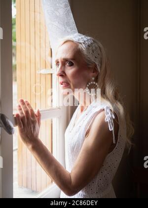 Portrait vertical d'une femme mûre et anxieuse debout et regardant à travers la fenêtre Banque D'Images