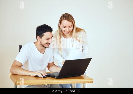 Un couple heureux vérifiant le compte bancaire sur un ordinateur portable, assis sur le bureau à la maison Banque D'Images