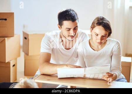 Le couple lit les instructions pour l'assemblage de meubles dans une nouvelle maison avec des boîtes mobiles sur l'arrière-plan Banque D'Images