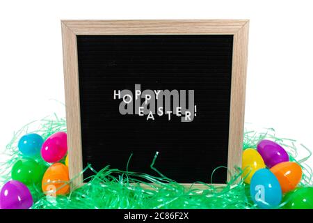 Un panneau noir avec un cadre de bouleau qui dit joyeuses Pâques dans des lettres blanches avec des oeufs de Pâques colorés dispersés derrière lui sur un fond blanc pur Banque D'Images