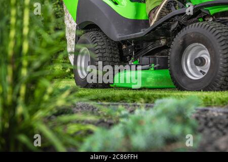 Thème aménagement paysager et jardinage. Fauchage de l'herbe de jardin à l'aide d'un tracteur de jardin à équitation professionnel. Banque D'Images