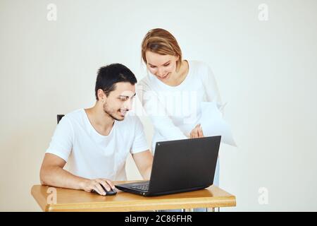 Un couple heureux vérifiant le compte bancaire sur un ordinateur portable, assis sur le bureau à la maison Banque D'Images