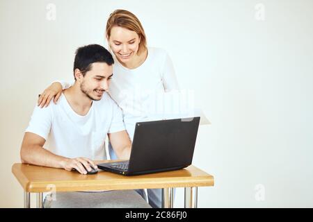 Un couple heureux vérifiant le compte bancaire sur un ordinateur portable, assis sur le bureau à la maison Banque D'Images