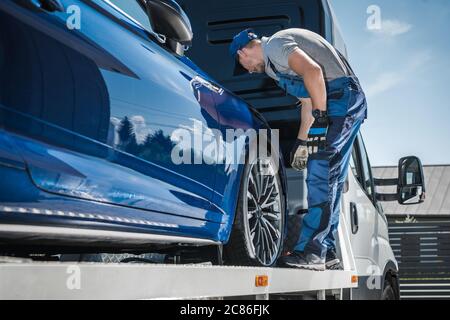 Un travailleur de reprise de possession de voiture sécurisant le véhicule sur son camion de remorquage. Société de financement de véhicules et de repo. Banque D'Images