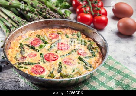 Frittata fait d'oeufs, d'asperges et de tomates cerises sur une poêle. Cuisine italienne Banque D'Images