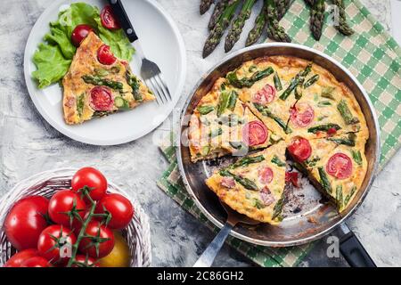 Frittata fait d'oeufs, d'asperges et de tomates cerises sur une poêle. Cuisine italienne Banque D'Images