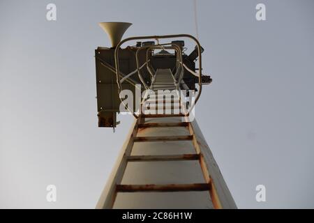 Vue du bas sur l'échelle au mât avant avec corne sur le navire à conteneurs marchand en début de soirée en été avec ciel sans nuages. Banque D'Images