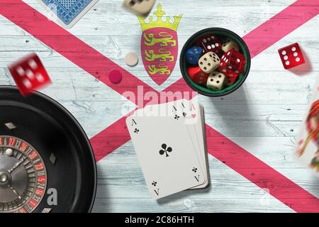 Thème casino Jersey. Jeu de poker, cartes et jetons sur table rouge avec fond de drapeau national. Jeux et Paris. Banque D'Images