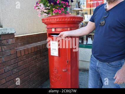 Man affiche une lettre dans une case rouge à l'entrée du bureau de poste de la rue Welsh au Royaume-Uni. Banque D'Images