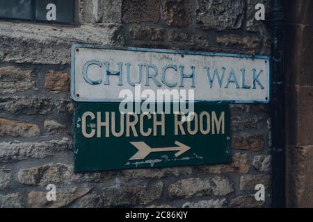 Rue signe et une flèche directionnelle à la salle d'église sur un bâtiment en calcaire sur l'église de la promenade à Stow sur le Wold, Cotswolds, UK, sélectif foyer. Banque D'Images
