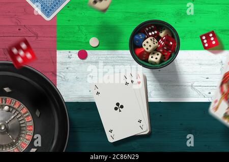Thème du casino des Émirats arabes Unis. Jeu de poker, cartes et jetons sur table rouge avec fond de drapeau national. Jeux et Paris. Banque D'Images