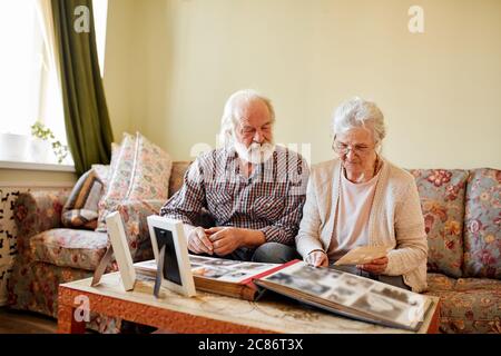 Souvenirs sentimentaux. Couple senior assis à la maison sur un canapé d'époque passant par les anciens albums photo, pensant à des jours passés. Banque D'Images