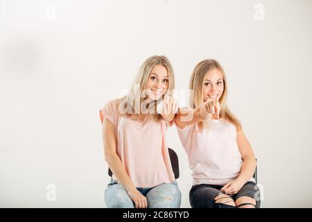 Deux sœurs gaies et attratives jumeaux pointant sur fond blanc. Banque D'Images