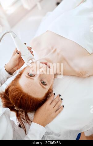 Cosmétologie matérielles. Close up photo de belle femme avec du gingembre frais et de cheveux la peau de rousseur recevant rf mode élévation dans un centre de beauté. Banque D'Images