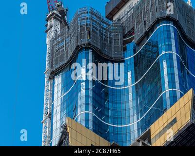 Vue détaillée d'un immeuble de luxe en construction. Verre doré et bleu. Machines, échafaudages, grues et autres équipements de construction. Banque D'Images