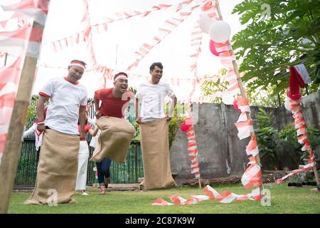 Trois jeunes hommes se sont joints à la course de sacs sautant rapidement pour atteindre la ligne d'arrivée à la célébration du 17 août de la Journée de l'indépendance indonésienne Banque D'Images