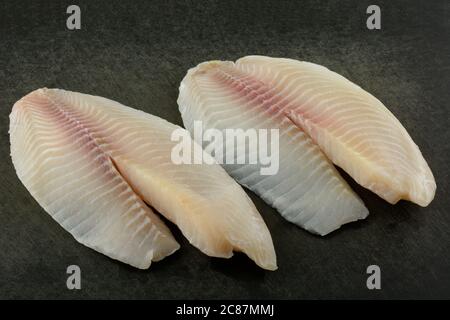 Filets de poisson frais et crus de tilapia sur une planche à découper noire abîmé Banque D'Images