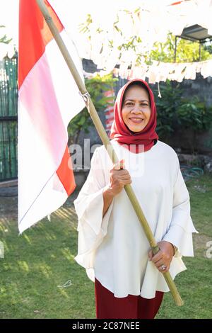 Grand-mère hijab tenant un bâton de bambou marqué d'Indonésie pendant la célébration de l'indépendance indonésienne en plein air Banque D'Images