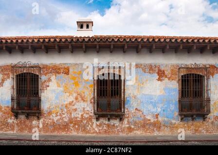 Façade de maison de style colonial dans la ville de la Antigua Guatemala, avec cheminée et balcons en fer forgé, rue pavée et ciel bleu. Banque D'Images