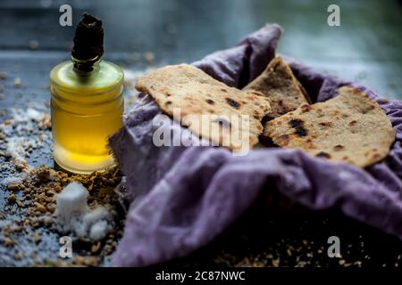 Grenaille de bhakri dans un récipient en panier avec un peu de farine de blé étalée sur la surface et un peu d'huile de cuisson dans une petite bouteille en verre sur une couleur noire Banque D'Images