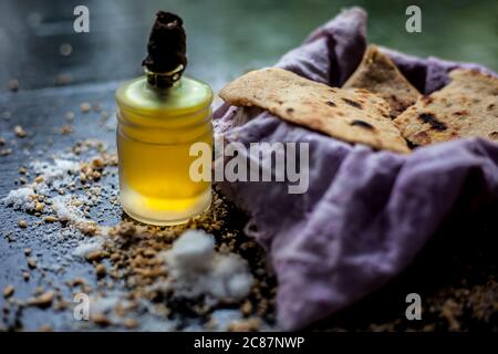 Grenaille de bhakri dans un récipient en panier avec un peu de farine de blé étalée sur la surface et un peu d'huile de cuisson dans une petite bouteille en verre sur une couleur noire Banque D'Images