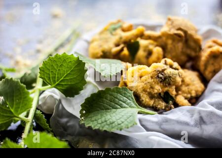 Gros plan de la collation de mousson ajwain pakora dans un récipient avec une feuille fraîche d'ajwain avec elle sur une surface avec un peu de farine de pois chiches saupoudrées Banque D'Images