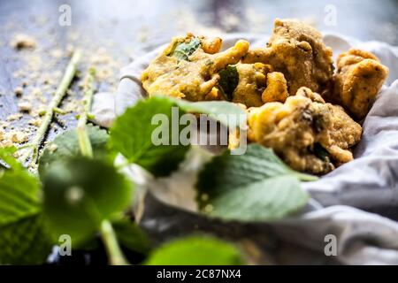 Gros plan de la collation de mousson ajwain pakora dans un récipient avec une feuille fraîche d'ajwain avec elle sur une surface avec un peu de farine de pois chiches saupoudrées Banque D'Images