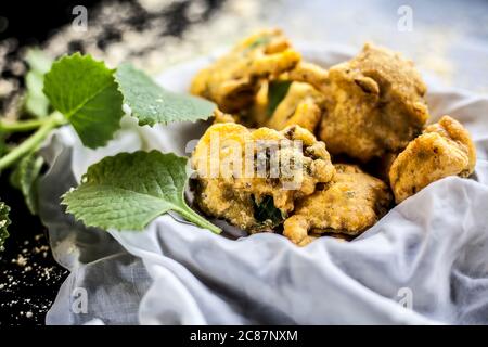 Gros plan de la collation de mousson ajwain pakora dans un récipient avec une feuille fraîche d'ajwain avec elle sur une surface avec un peu de farine de pois chiches saupoudrées Banque D'Images
