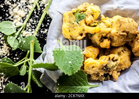 Gros plan de la collation de mousson ajwain pakora dans un récipient avec une feuille fraîche d'ajwain avec elle sur une surface avec un peu de farine de pois chiches saupoudrées Banque D'Images
