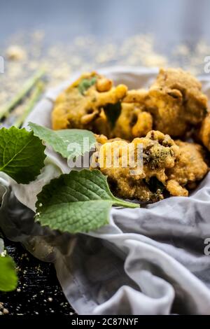 Gros plan de la collation de mousson ajwain pakora dans un récipient avec une feuille fraîche d'ajwain avec elle sur une surface avec un peu de farine de pois chiches saupoudrées Banque D'Images