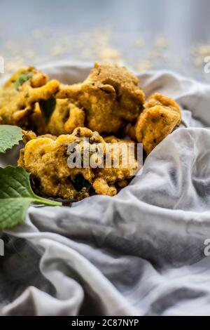 Gros plan de la collation de mousson ajwain pakora dans un récipient avec une feuille fraîche d'ajwain avec elle sur une surface avec un peu de farine de pois chiches saupoudrées Banque D'Images