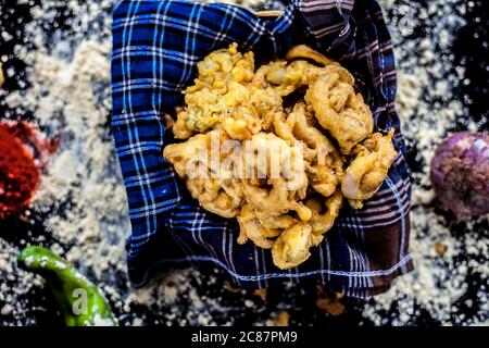 Célèbre Kanda bhaji ou Kanda bhajiya ou Kanda pakora dans un récipient sur une surface noire avec de la farine de pois chiches, des épices, des oignons, et tous les autres ingrédients Banque D'Images