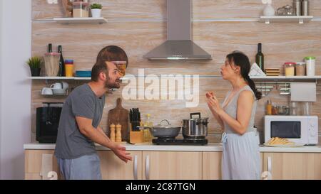 Couple criant les uns aux autres dans la cuisine le matin. Jeunes couples en querelle dans la cuisine. L'homme et la femme hurlent dans la frustration pendant la conversation à domicile. Banque D'Images