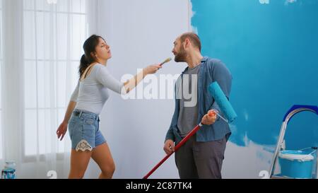 Fille chantant sur la brosse de peinture et de décoration d'appartement avec l'aide de mari gai. Rénovation d'appartements et construction de maisons tout en rénove et en améliorant. Réparation et décoration. Banque D'Images