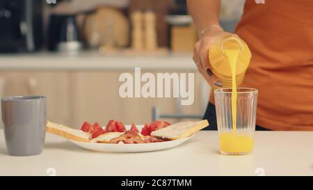 Femme versant du jus frais dans le verre pour le petit déjeuner dans la cuisine. Femme qui boit du jus d'orange sain et naturel. Femme au foyer boire du jus d'orange maison sain et naturel. Rafraîchissement le dimanche matin Banque D'Images