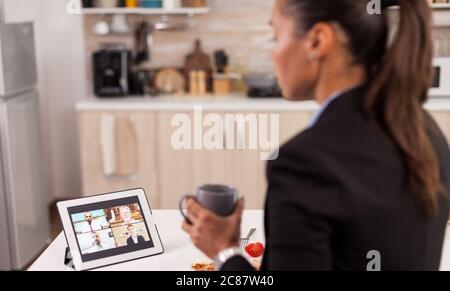 Femme d'affaires le matin ayant une conférence téléphonique en ligne tout en prenant le petit déjeuner dans la cuisine. Banque D'Images