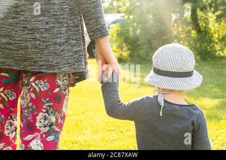 Bonne famille dans le parc lumière du soir. Silhouette mère et bébé marchant au coucher du soleil. Le concept d'une famille heureuse. La mère tient la main du bébé. Papillon Banque D'Images