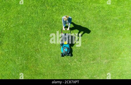 Belle fille coupe la pelouse. La tonte du gazon. Vue aérienne belle femme tondeuse sur l'herbe verte. Équipements de l'herbe de la faucheuse. Le travail de soins de jardinier tonte Banque D'Images