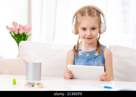 Belle petite fille avec tablette blanche avec casque, dans la chambre Banque D'Images