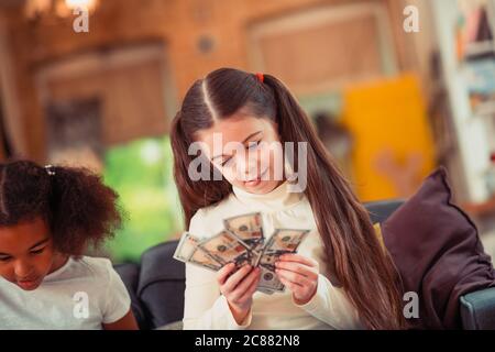 Petite fille concentrée regardant des billets de banque en dollars Banque D'Images