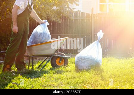 Le jardinier d'homme met des sacs de compost dans le chariot. Uniforme vert. Léger. Banque D'Images