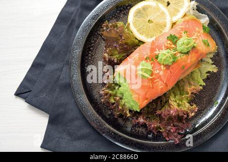 Saumon fumé rempli de purée de pois sur salade de laitue avec tranches de citron et garniture de persil sur une assiette et une serviette sombres, table blanche, carb de vache sain ou Banque D'Images