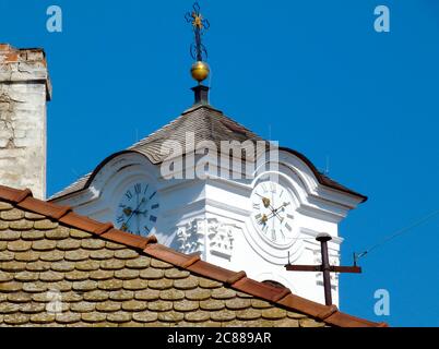 Tour d'horloge en stuc blanc avec cadran rond et poignées noires. Toit en argile et arête anciens. Ciel bleu. Croix noire et or Banque D'Images