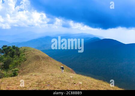 Un homme de randonnée avec un poteau de randonnée sur le sommet de la montagne, nuages bleus magiques et chaîne de montagnes dans les arrière-plans. Banque D'Images