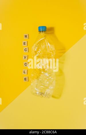 Image couleur verticale avec vue en hauteur d'une bouteille en plastique transparente et écrasée avec capuchon bleu sur fond jaune et le mot recycle. Recy Banque D'Images