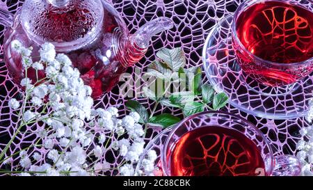 Une tasse de thé rouge en fleurs d'hibiscus blanc et des feuilles vertes de thé médicinal sur un stand en bois.cérémonie de thé Zen. Photo de la guérison indienne à base de plantes rouges Banque D'Images